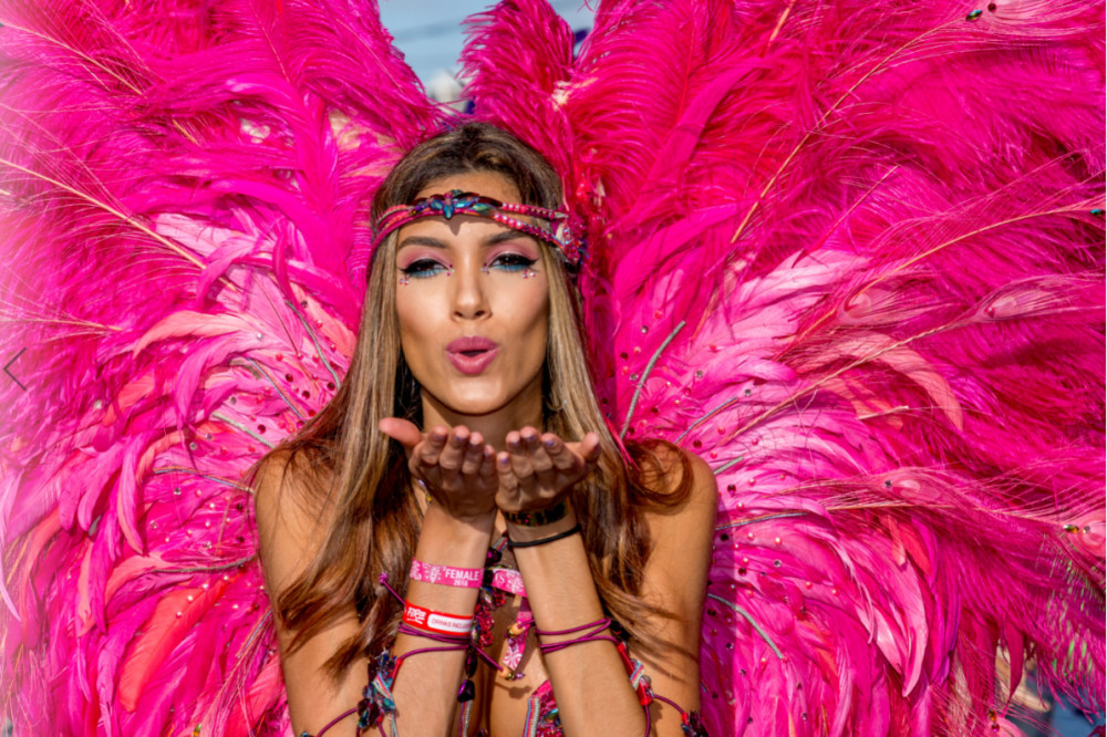 Young lady in Carnival costume with pink backpack blowing a kiss with both palms up and open in front of her