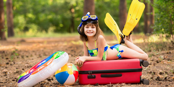 girl in swimsuit, fins and swimming mask with circle and swimming ball packed suitcase, and ready to fly for summer vacation trip in the Caribbean