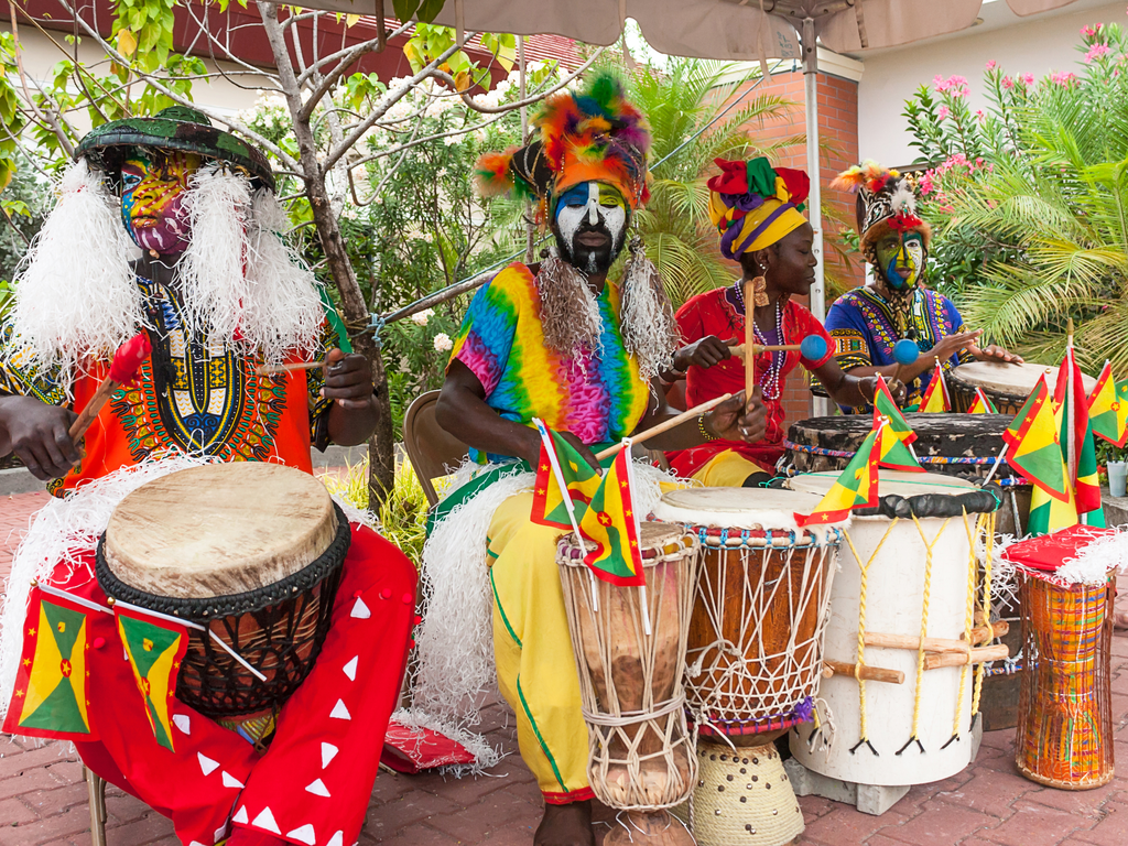 Musicians dress with typical costumes and makeup are playing African drums in St. Georges Habrour (Grenada) answering the question is it safe to travel to Caribbean with a thumping yes.