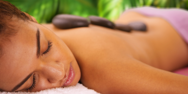 A young lady with eyes closed laying on her stomach enjoying a hot stone massage