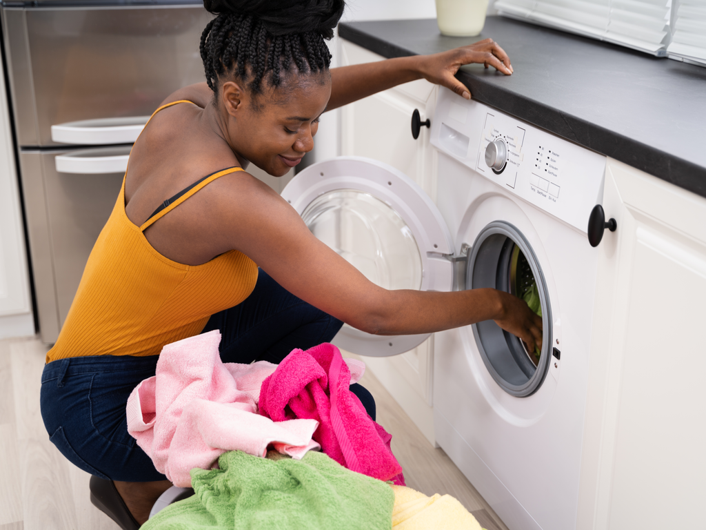 A young lady in yellow spagetti strap top and black pants taking clothes out of the dryer