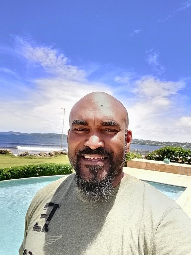 Smiling Black man in green top on a sunny day with Atlantic ocean in the background