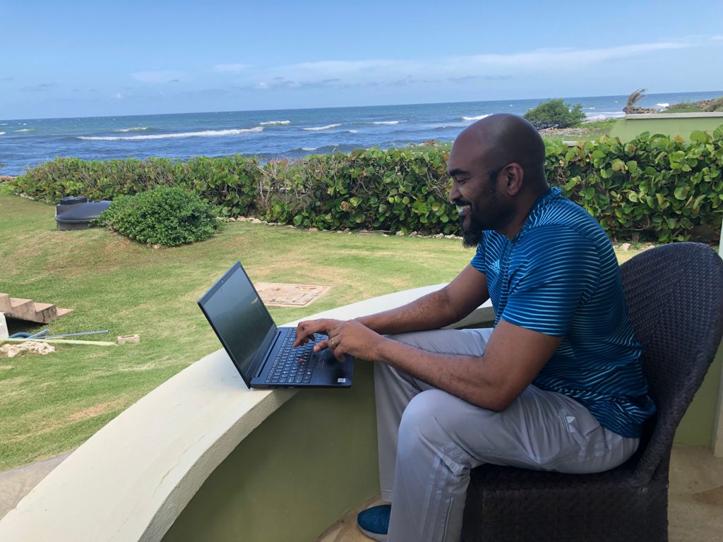 Black man sitting in relax wear smiling while working on laptop with Atlantic ocean in the foreground