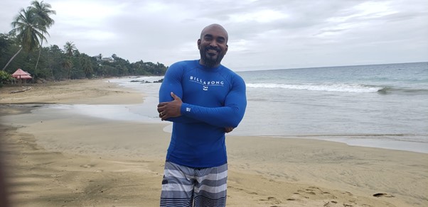 Black man on beach in blue Billabong long sleeve swim top and trunks