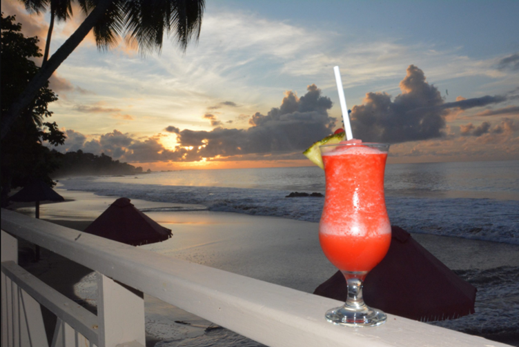 Pina colada cocktail on the banister of a beach bar with the sunset and beach in the background